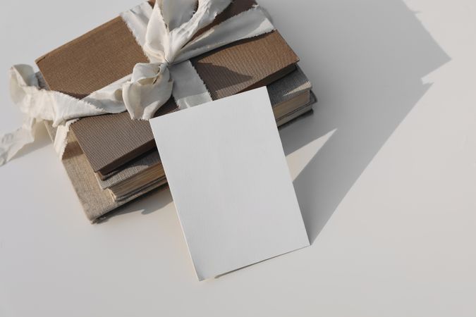 Blank greeting card on top of stack of books tied up with beige ribbon