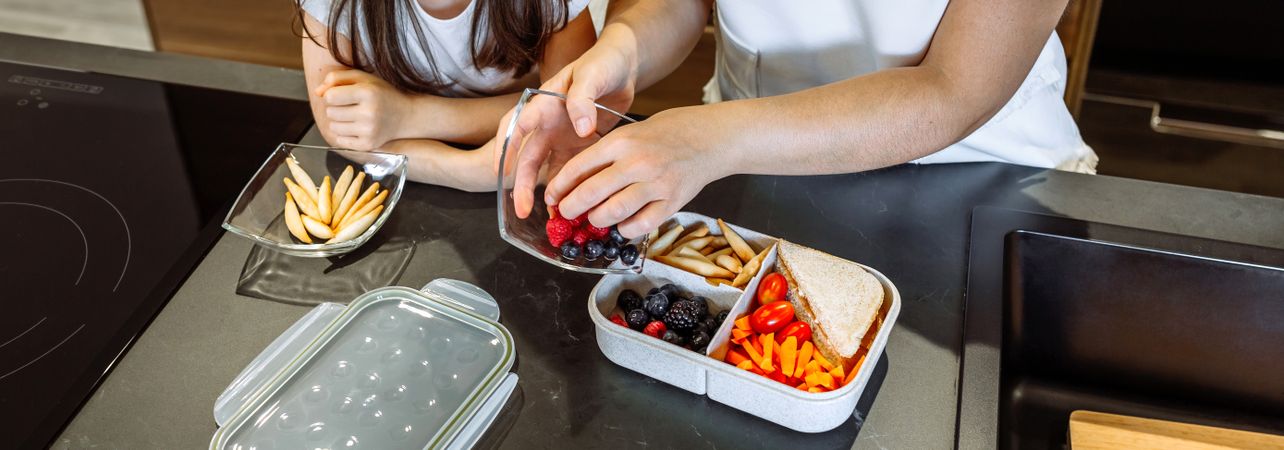 Girl watching her mother putting food in her lunch box