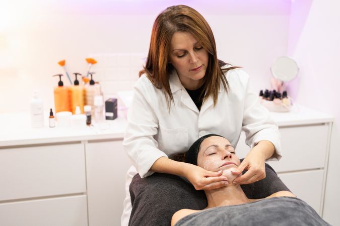 Beautician massaging face of female customer in beauty salon