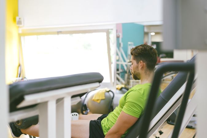 Looking through gym equipment at male in green t-shirt working out using machine