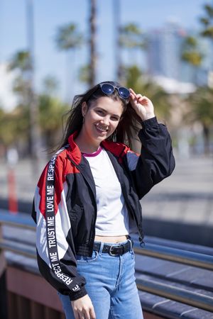 Front view of happy young woman adjusting glasses and looking at camera on sunny day