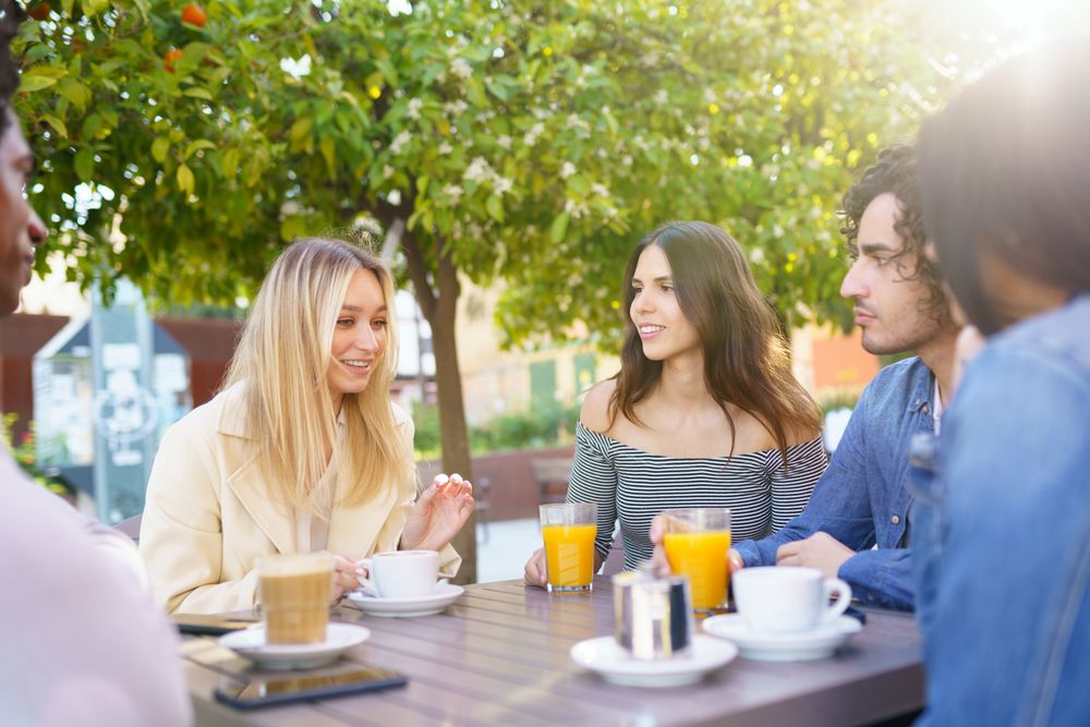 Diverse group of friends meeting up over coffee and juice at outside table