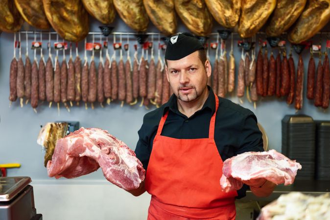Man holding chunks of ham behind counter in butcher shop