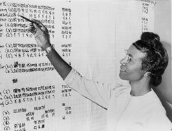 Shirley Chisholm, Congresswoman from New York, looking at list of numbers posted on a wall, 1965 4d2ON0