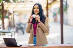 A woman enjoys coffee at a cozy cafe with her laptop and smartphone, her perfect workspace