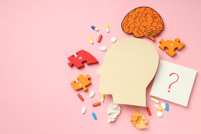 Paper cut out of side view of head with medications and puzzle pieces on pink background, copy space