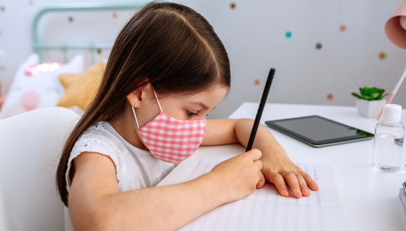 Girl with mask doing homework in her bedroom