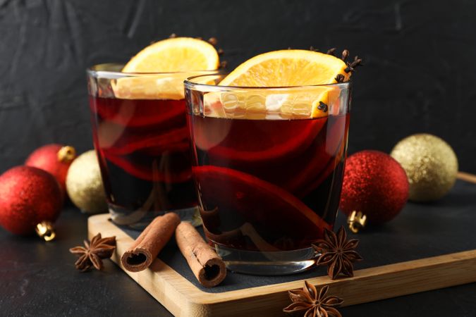 Glasses of tasty mulled wine and christmas baubles on dark background, close up
