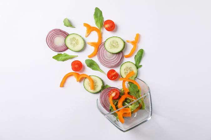 Glass bowl with fresh vegetables slices on plain background, copy space