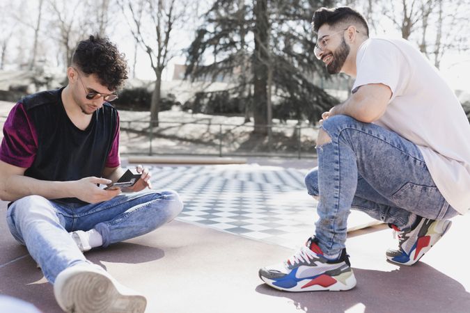 Handsome positive men using smartphone and sitting on floor in park