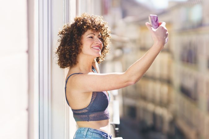 Smiling women taking picture with her phone on balcony