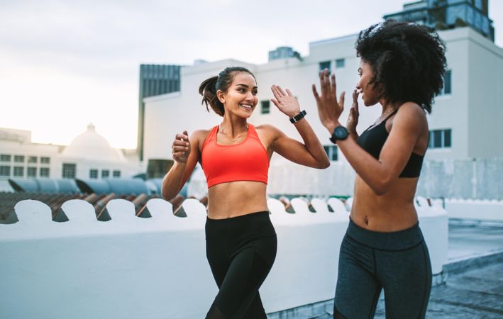 Two fitness women jogging on rooftop in the morning and giving high five