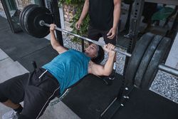 man lifting barbell with trainer