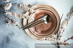 Top view of pink table setting of apricot blossom branches surrounding plates on grey table 5qkPNY