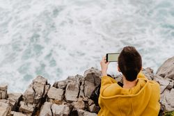 Woman in yellow hoodie taking selfie on smartphone on rocky shore