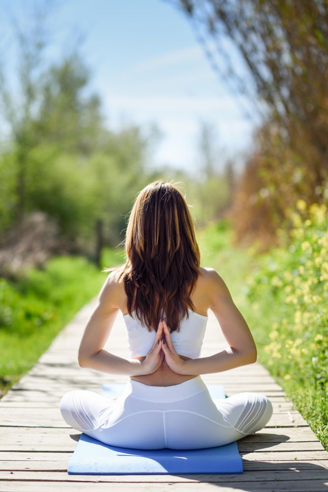 Back of female wearing light sport clothes meditating with arms behind her back, vertical