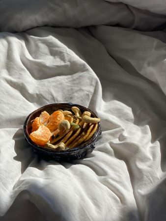 Breakfast bowl of fresh orange slices, nuts and mini pancakes in morning light