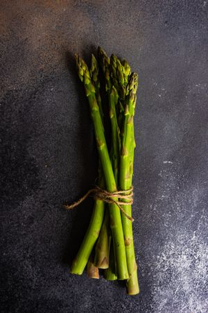 Wrapped bunch of raw asparagus on dark counter