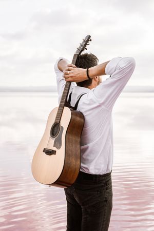 Musician gazing and carrying guitar behind back while standing on beach