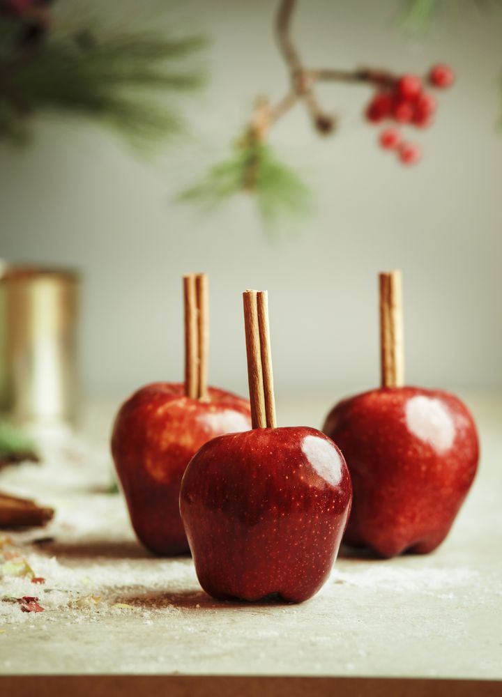Red apples with cinnamon sticks on kitchen table with sugar at wall background with fir green