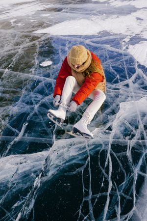 Woman sitting on frozen river and tying the shoelaces