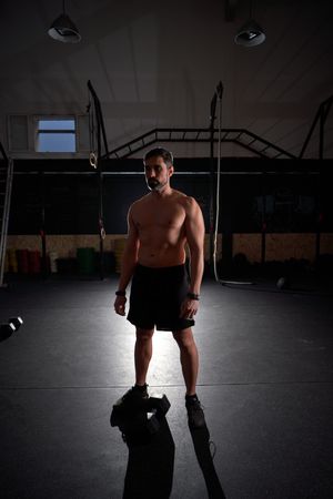 Shirtless sportsman standing in dark gym