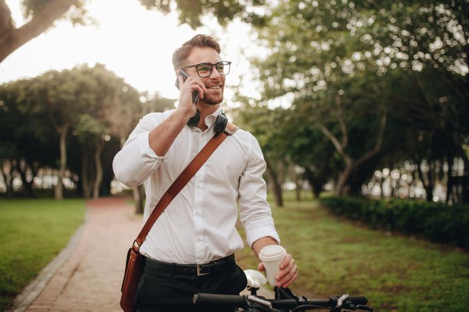 Smiling businessman talking over mobile phone standing on street with his bicycle