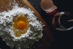 Broken egg and flour on black background