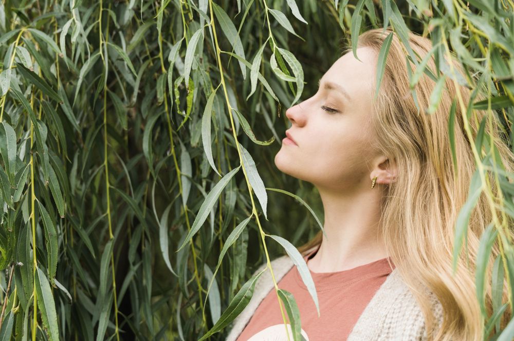 Side view of Blonde woman standing beside tree closing her eyes