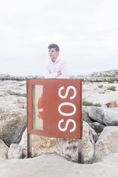 Young male teenager with arms crossed standing on promenade by emergency life jacket