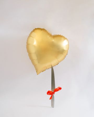 Heart balloon gold flying about to pierced with a sharp knife