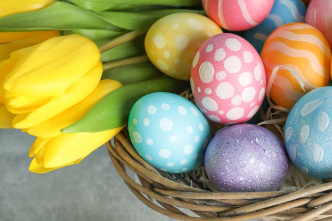 Easter basket filled with colorful eggs and flowers on a wooden background. Close up