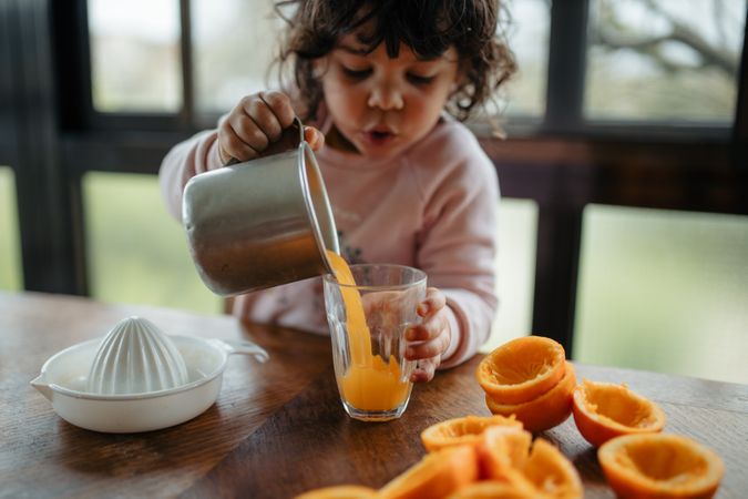 Little girl pouring fresh made juice into glass from small pitcher