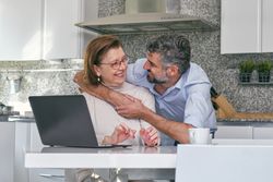 Adult son hugging senior mother at table with laptop
