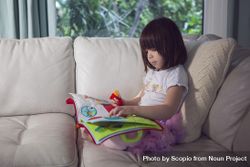 Girl holding children's book sitting on sofa 5RJMN5
