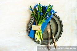 Top view of spring table setting with blue scilla siberica over blue napkin 0gXXkM