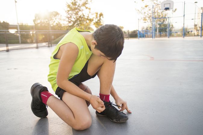 Teenager kneeling down tying shoes at street basketball court