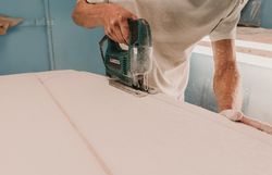 Man with tool sawing surf board in workshop