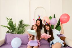 Family celebrating birthday with gifts and balloons on purple couch.