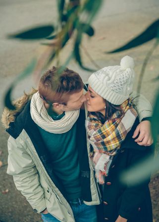 Cute couple in winter coats about to kiss under tree