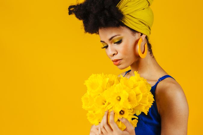 Portrait of thoughtful Black woman with large earrings holding a bouquet of daffodils