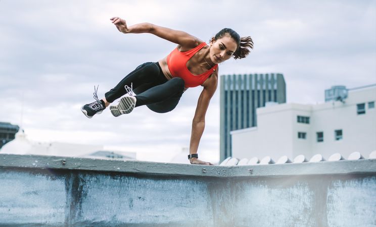 Female athlete jumping on to the rooftop from the roof fence taking support of one hand