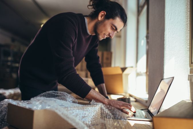 Young man working on laptop with parcel on the side