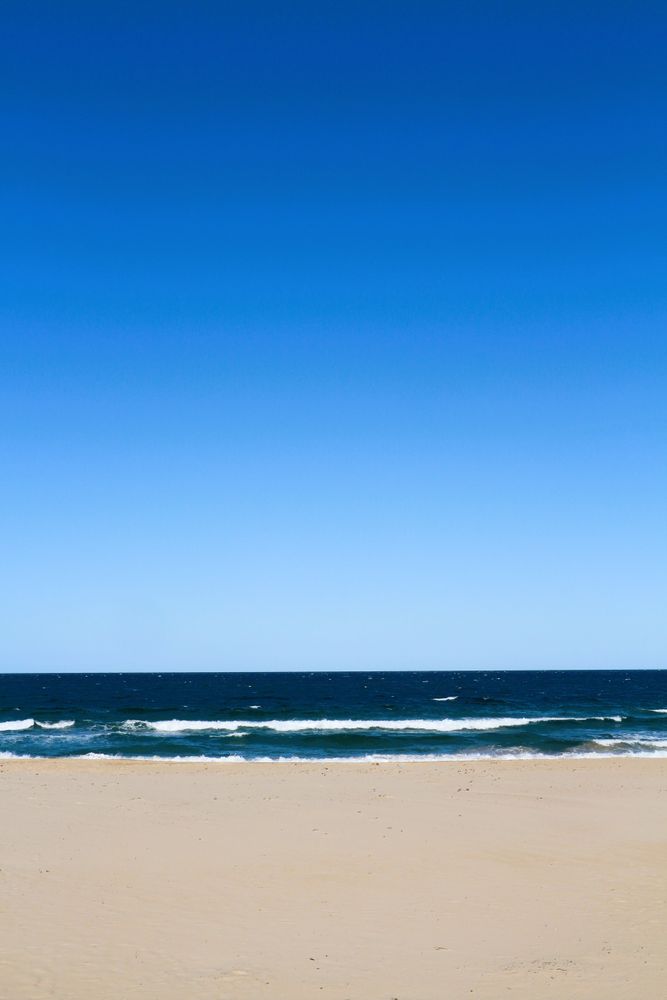 Calm beach under a clear blue sky with gentle waves lapping on the shore during a sunny day