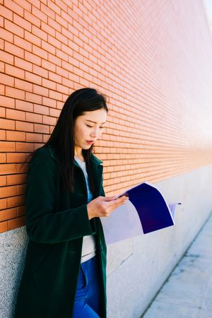 Asian student reading textbook near brick wall