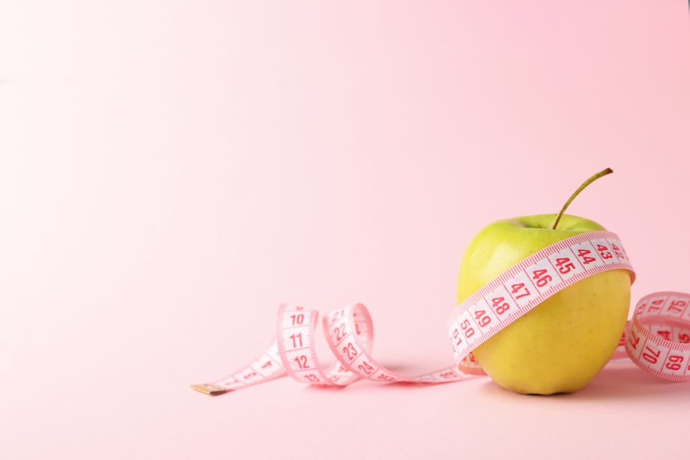 Measuring tape with apple on pink background, weight loss
