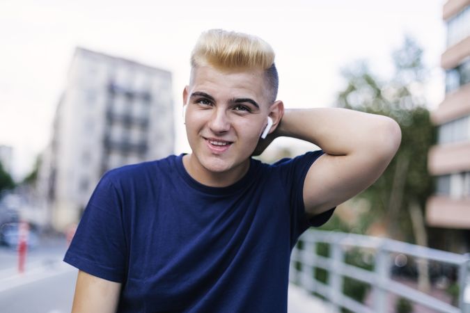 Portrait of young blond man with ear buds on the street while looking at the camera