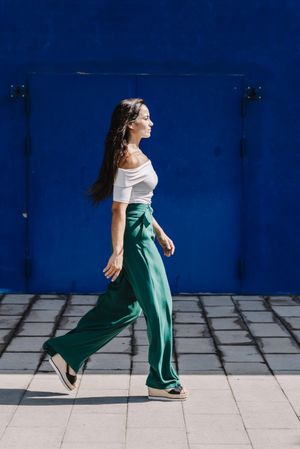 Young happy trendy woman walking in city against blue door