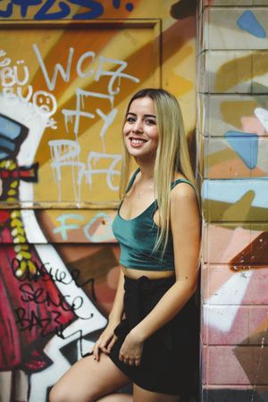 Stylish woman in sunglasses posing at graffiti wall on city street.