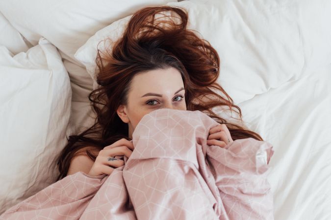Woman looks up from under pink blanket